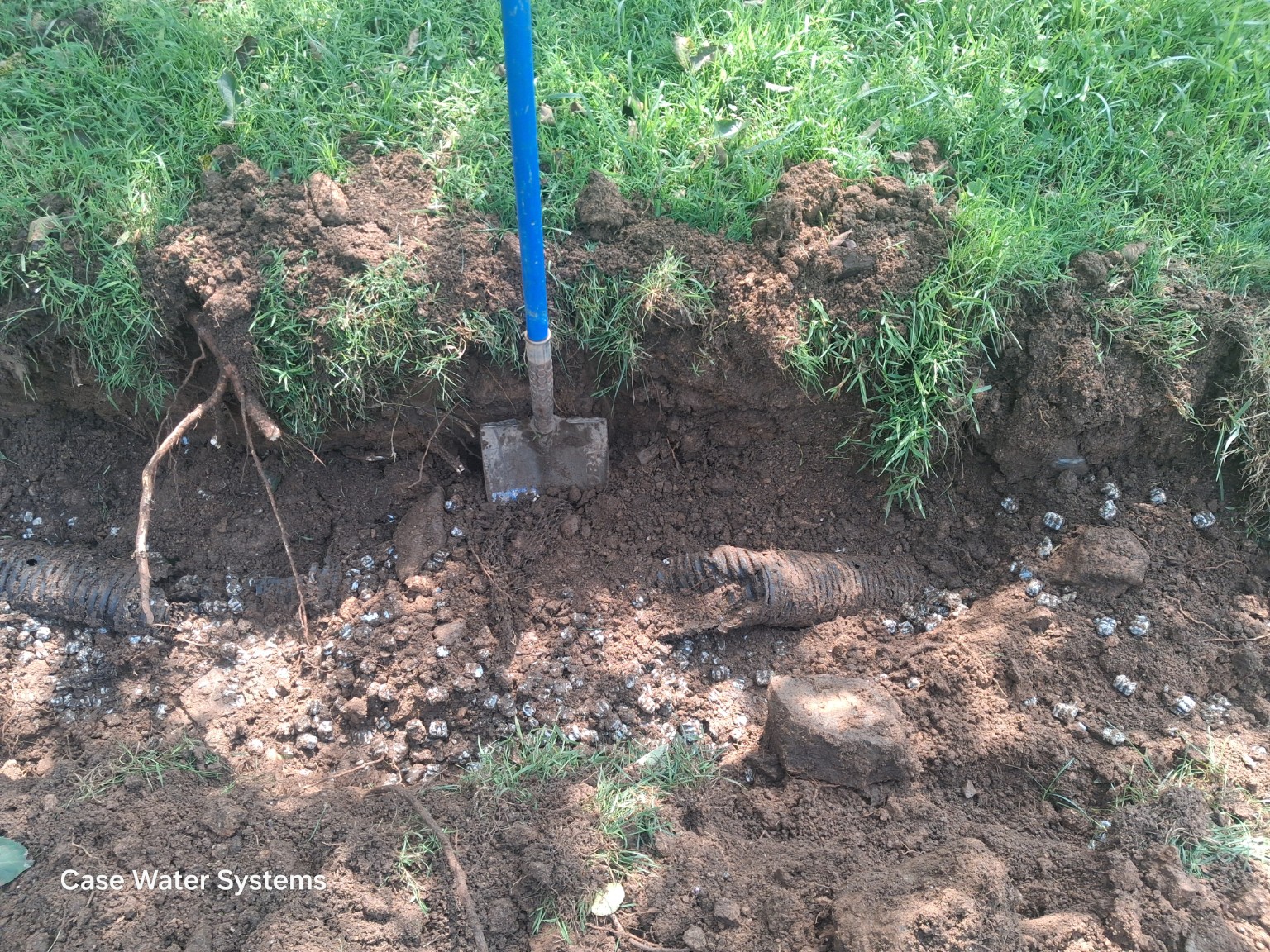 Excavated trench exposing piping and gravel.