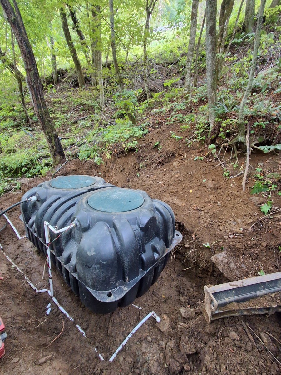 Tank placement on an excavated wooded hillside.