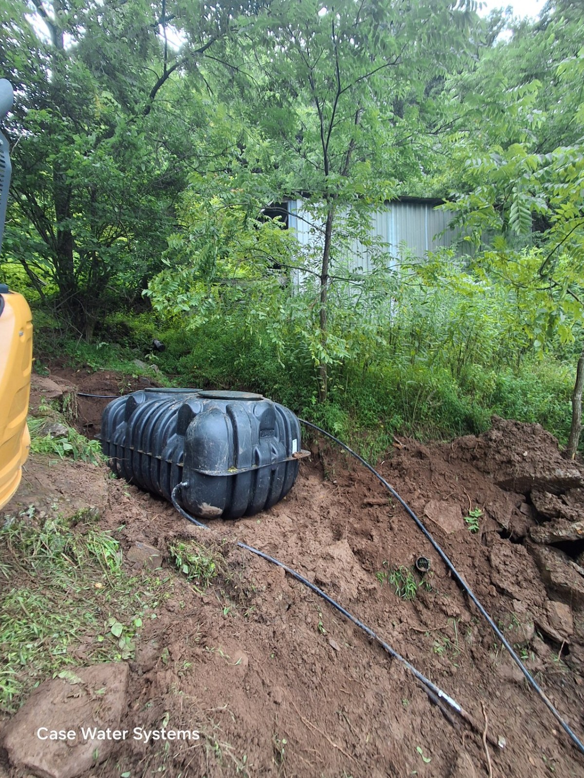 Black water storage tank beside an excavated hillside with connecting pipes